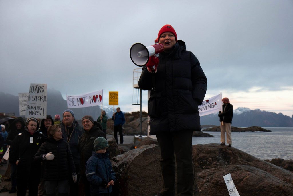 Mona Fagerås med en ropert i hånda. I bakgrunnen står flere med bannere for å protestere mot en mulig nedlegging av Kunst-og filmhøgskolen i Kabelvåg.Bilde