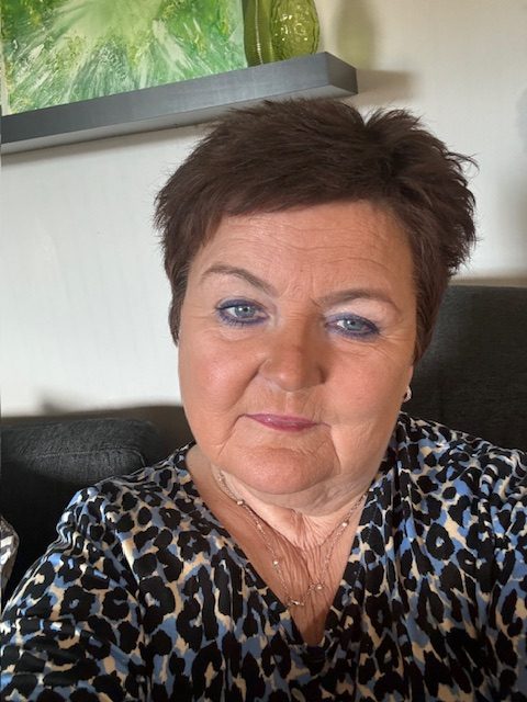 Iren-Marie Owe.Portrettbilde av Iren Marie Owe. I bakgrunnen kan man se en sofa og en hylle med et abstrakt maleri.