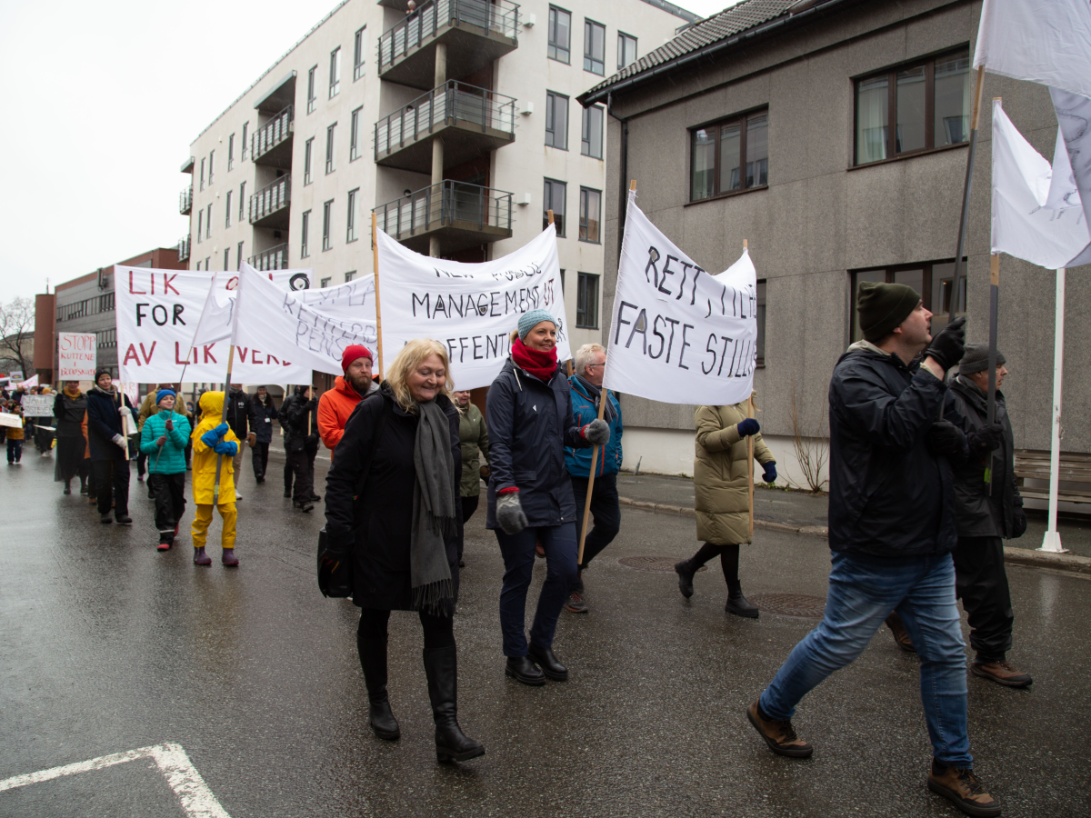 Bildet viser et 1.maitog hvor de som går i toget holder paroler. I bakgrunnen ser man flere bygninger. Bilde