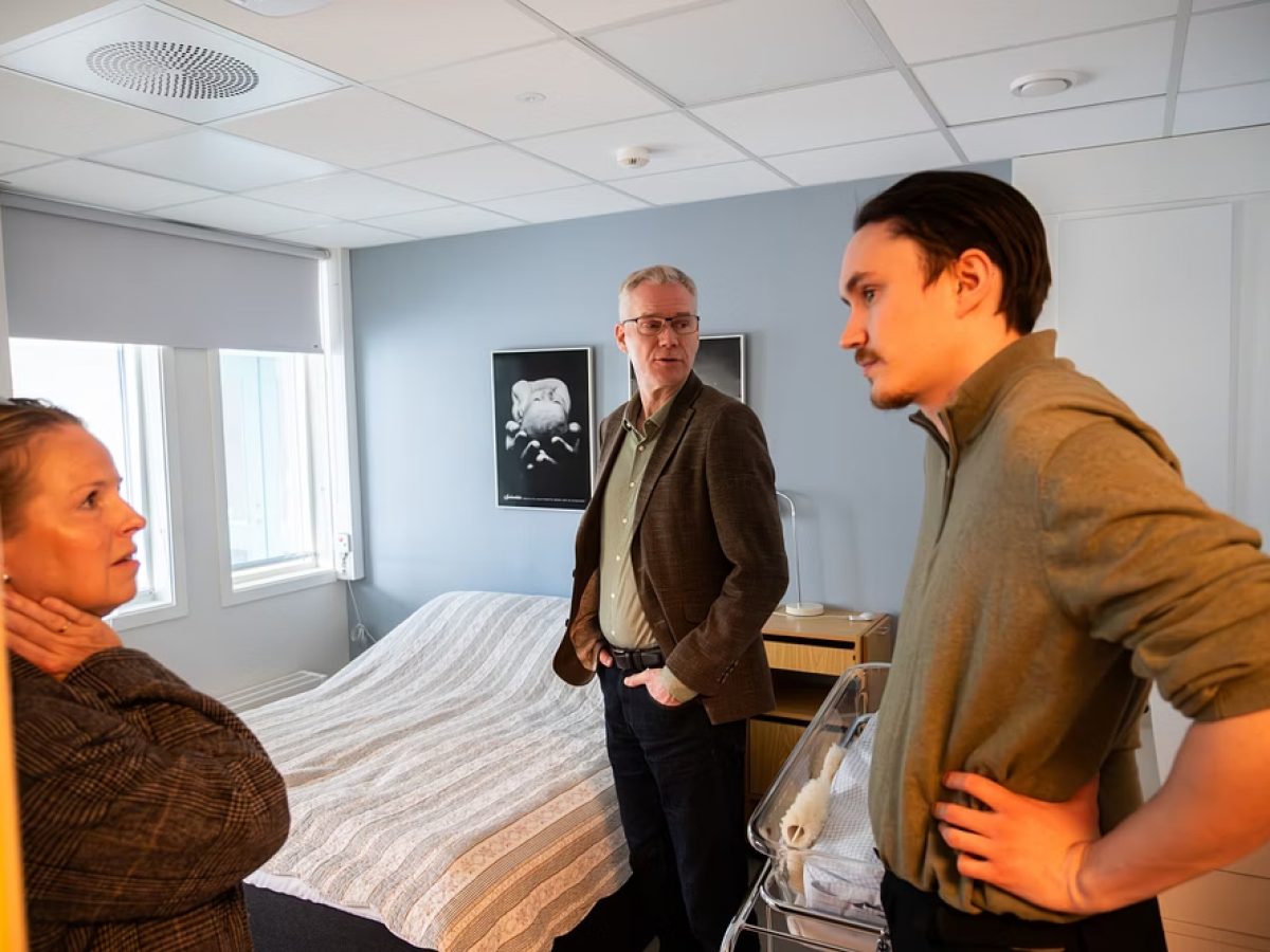 Ola Mathias Grotnes og Christian Torset prater med en av de som jobber på fødestua i Brønnøysund. I bakgrunnen kan man se en seng.